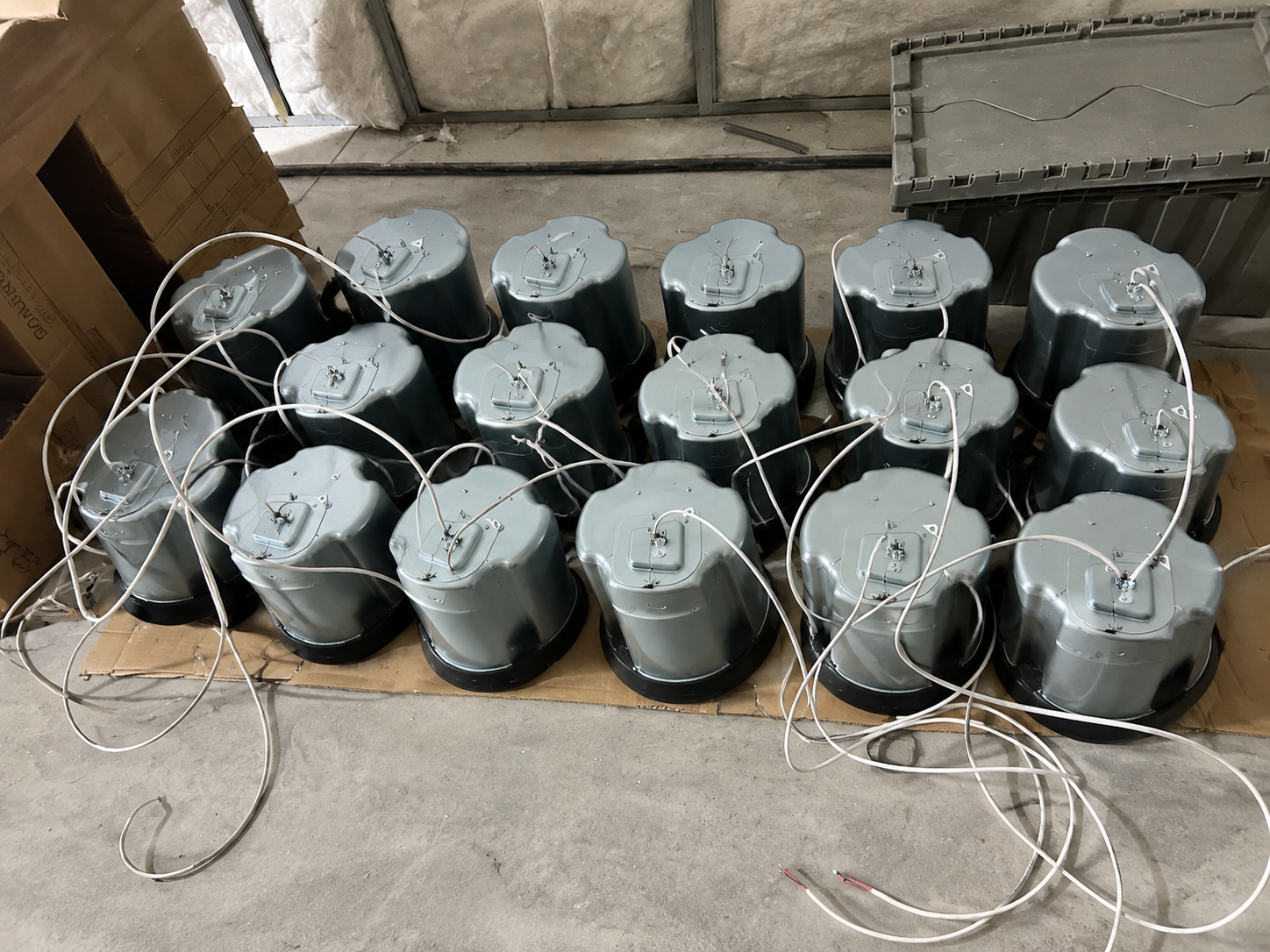 Seventeen ceiling speakers with white leads arranged on cardboard at an unfinished construction site.