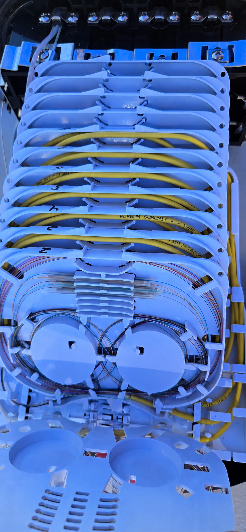 Open fiber enclosure containing organized splice trays, yellow fiber cables, and individual colored strands.