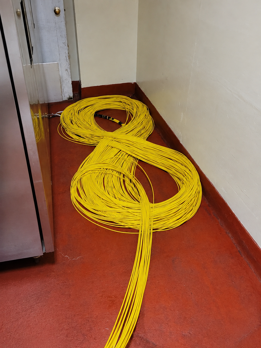 Multiple yellow fiber-optic cables staged in a figure-eight pattern on the floor of a cramped commercial kitchen.