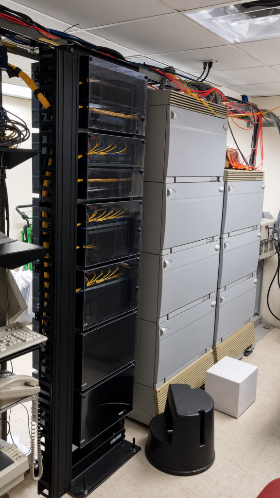New fiber-optic distribution racks installed beside a large legacy copper telephone system during a parallel infrastructure migration.